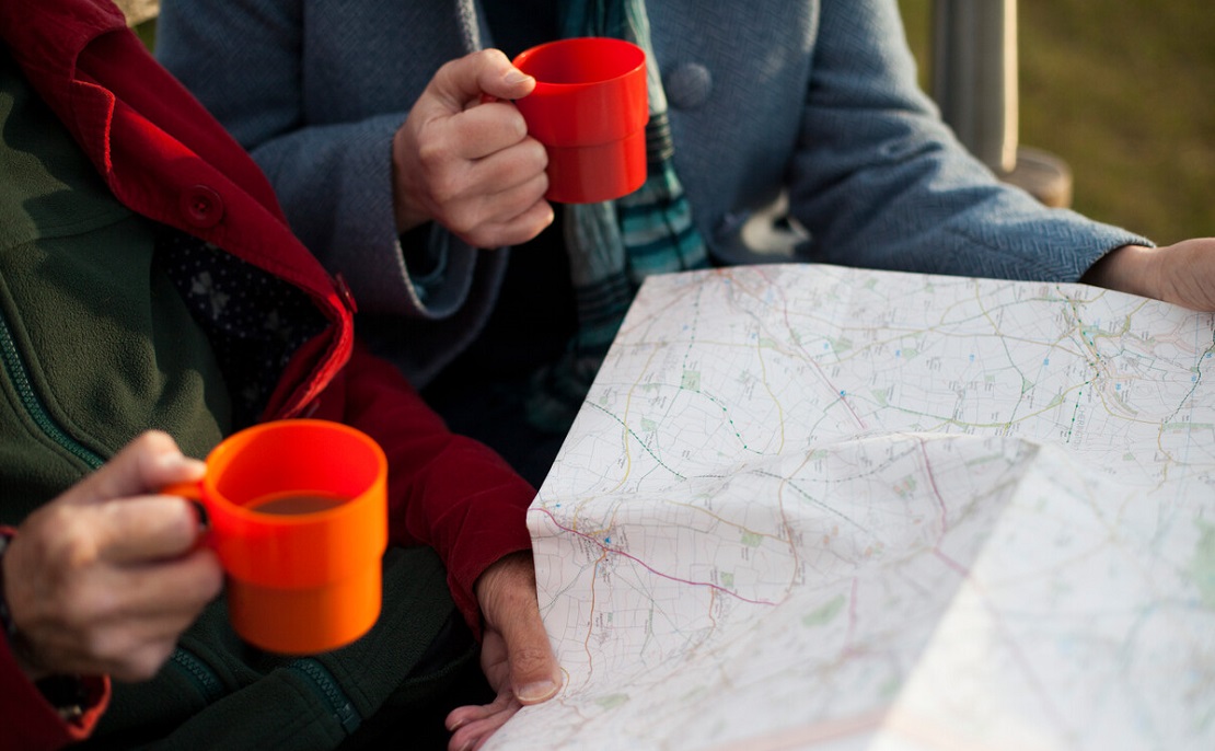 Women's hands holding mugs of coffee with a map spread out in front of them.