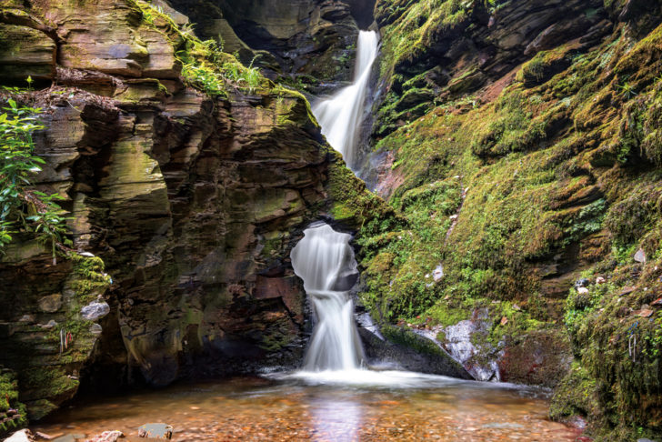 Waterfall cascading into pool below surrounded by moss covered rocks