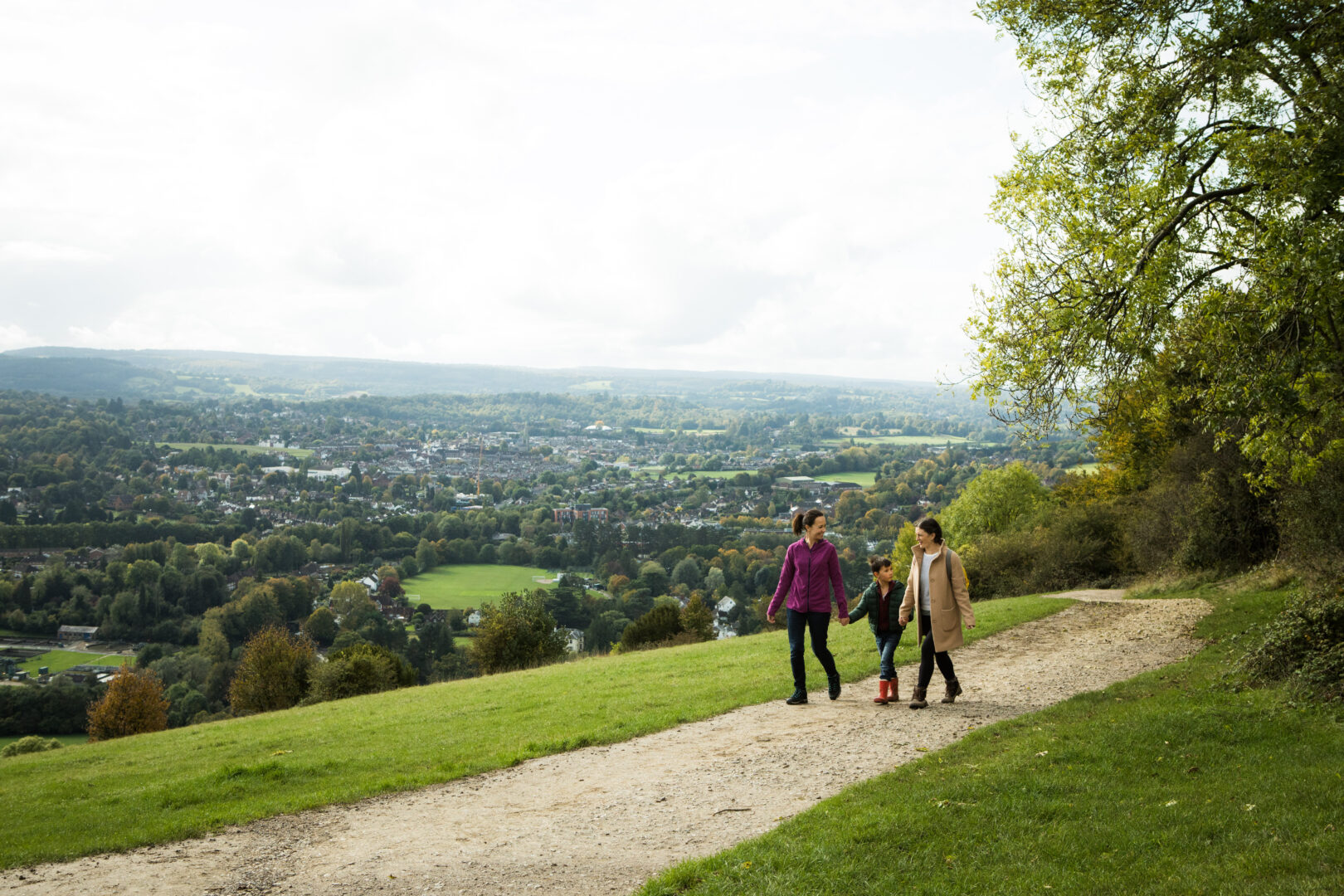 Two women and young boy walking along woodland footpath with view of fields in Surrey Hills AONB