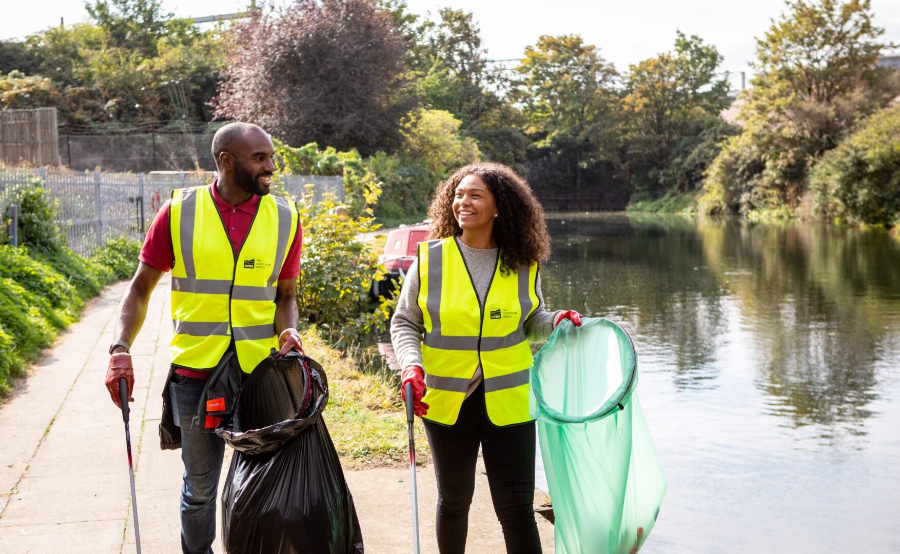 Man and woman in hi-vis jackets walking along canal litter pick