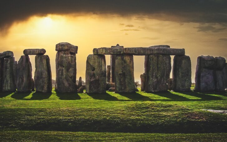 Stonehenge at sunset under a moody, cloudy sky, casting long deep shadows