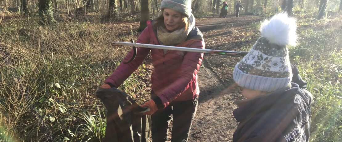 A child with an adult picking up litter in the woods on a sunny day