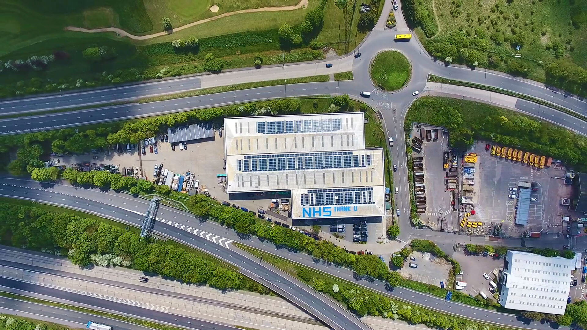Aerial photo of solar panels on warehouse roof in between two roads