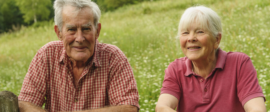 John Whetman and Audrey Compton leaning over a gate, with their wildlife rich grassland in the background