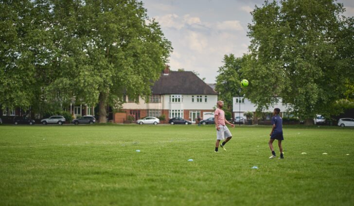 Two people playing football in a local green space