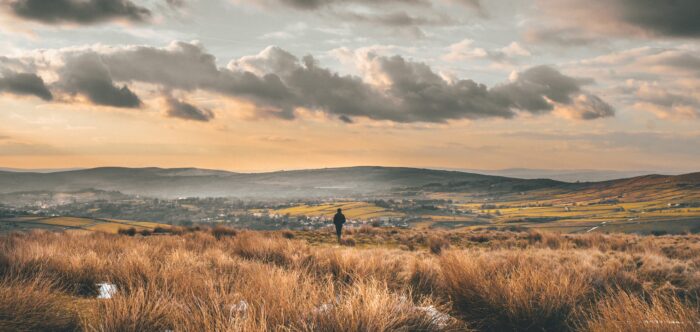 Person walking in hilly landscape with town in the distance