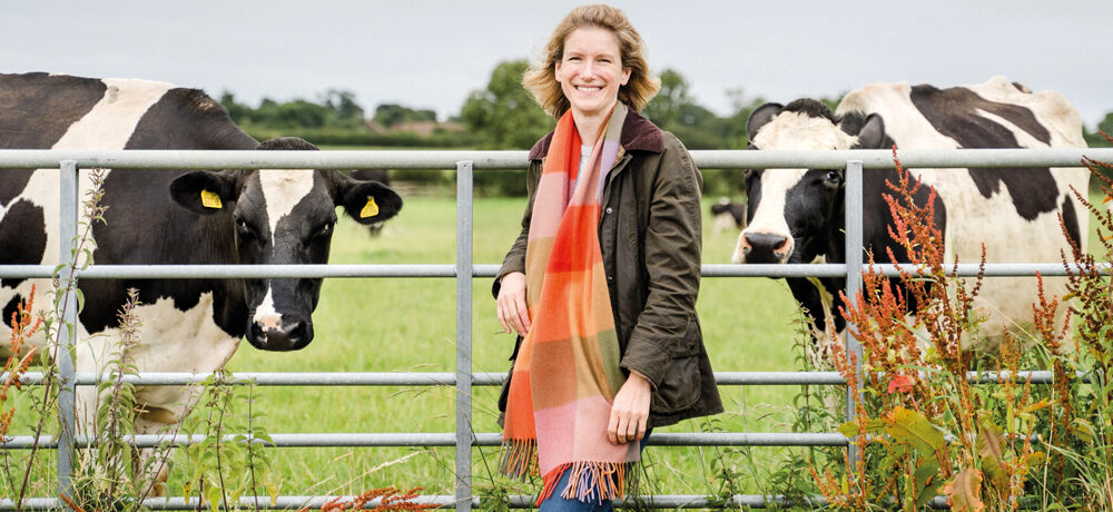 Ruth Grice on her farm stood in front of a metal gate with cows behind it