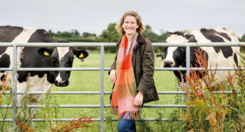 Ruth Grice on her farm stood in front of a metal gate with cows behind it