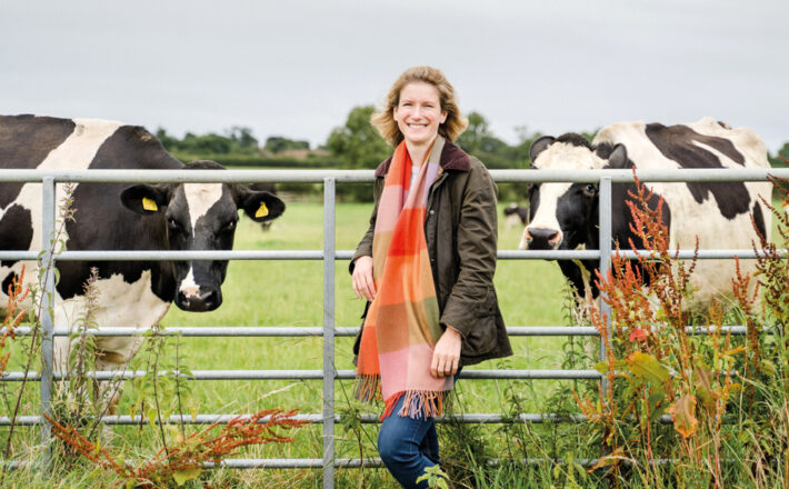 Ruth Grice on her farm stood in front of a metal gate with cows behind it