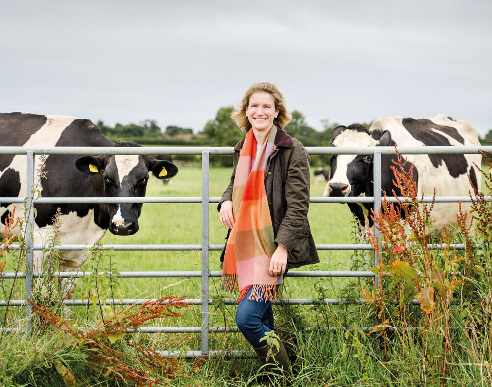 Ruth Grice on her farm stood in front of a metal gate with cows behind it