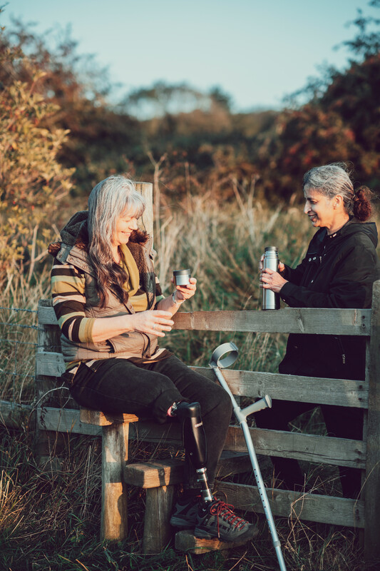 Two people sat at a stile with a hot drink