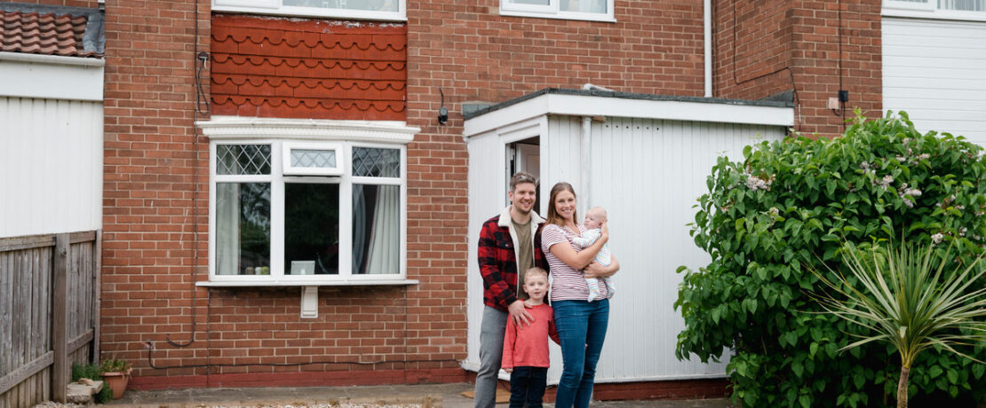 Family standing in front of a house and smiling