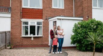 Family standing in front of a house and smiling