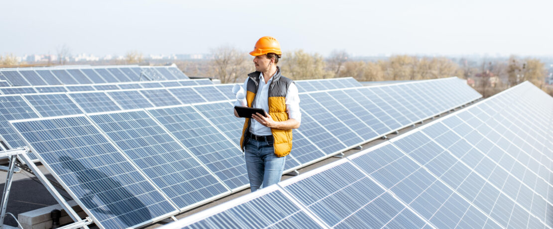 View on the rooftop solar power plant with man walking and examining photovoltaic panels. Concept of alternative energy and its service