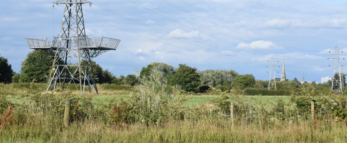 Pylons in the countryside with a church spire in the distance