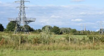 Pylons in the countryside with a church spire in the distance