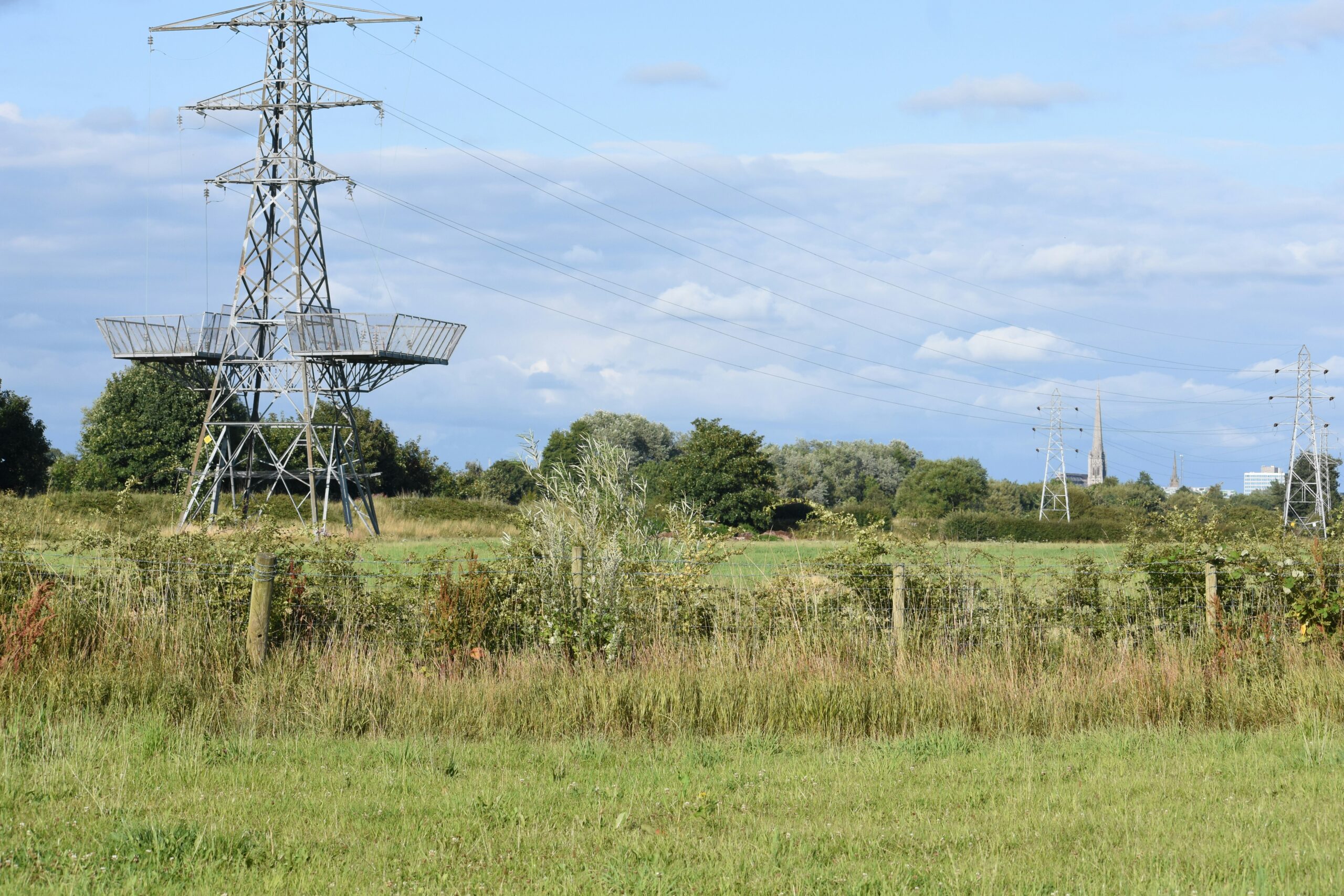 Pylons in the countryside with a church spire in the distance