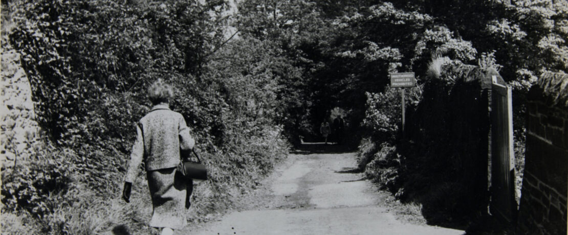 Black and white photo of Ethel Haythornthwaite walking down a country lane