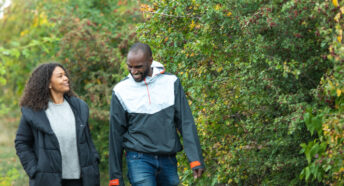 Happy couple walking along path with hawthorn hedgerow smiling