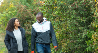 Happy couple walking along path with hawthorn hedgerow smiling