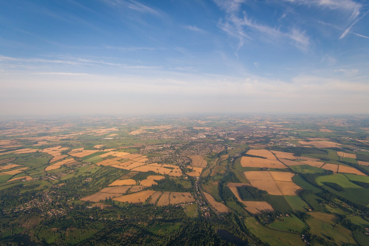 A wide horizon view of sky and fields with hedgerows and farmland