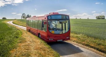 A photo of a red bus on a countryside lane