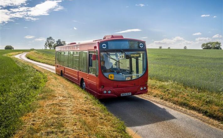 A photo of a red bus on a countryside lane