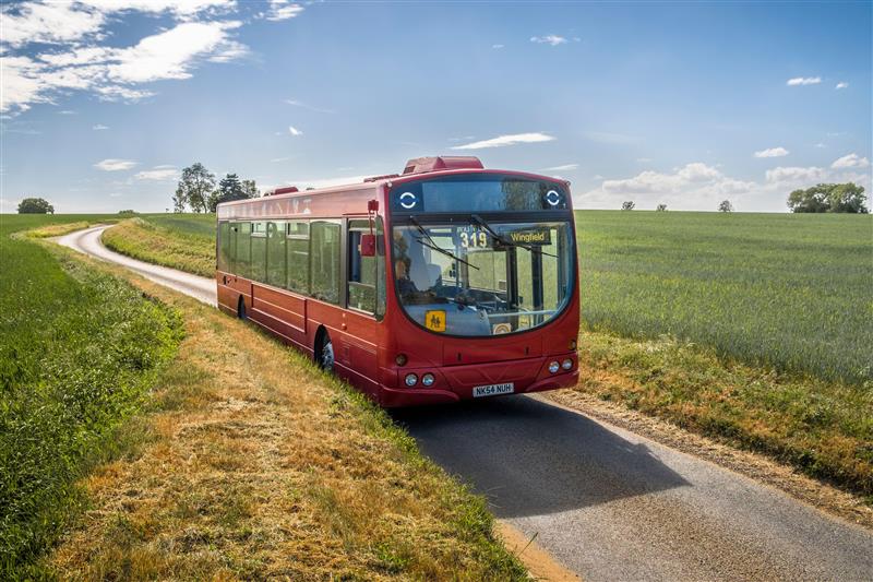 A photo of a red bus on a countryside lane