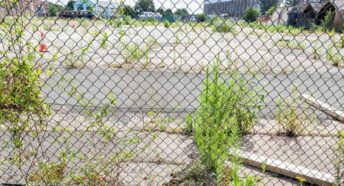 Unused brownfield site seen through wire fencing