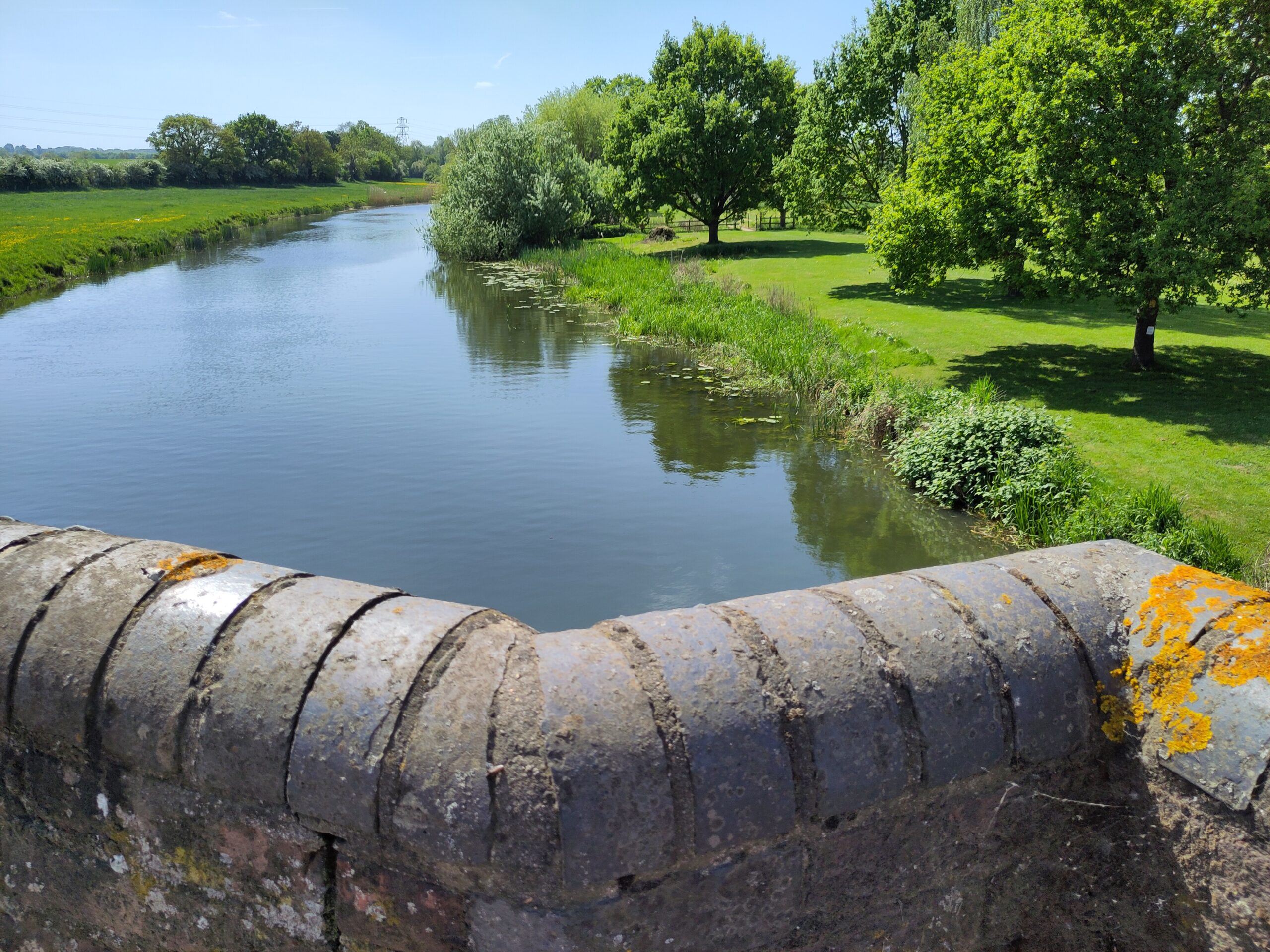 A wide calm river, lined with greenery, seen from a bridge.