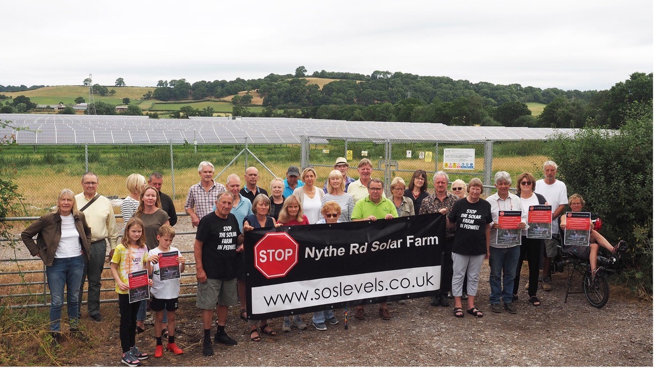 a group of people holding a banner in front of a solar farm